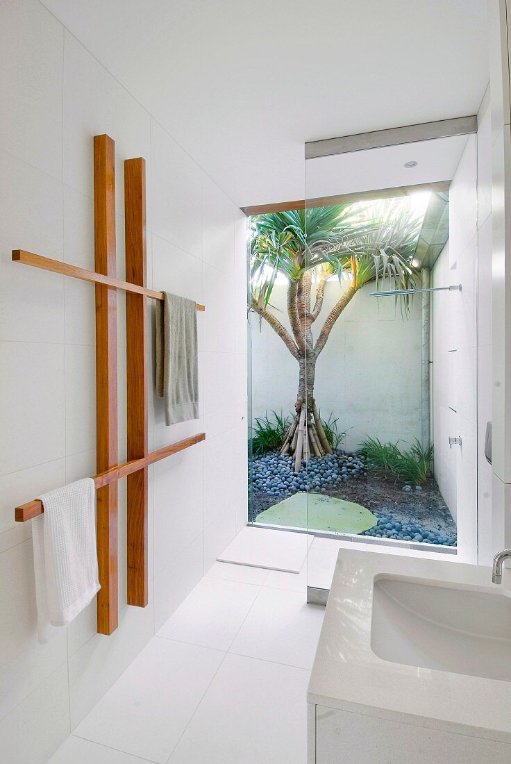 Weisses Designerbad mit abgetrenntem Duschbereich vor Glaswand mit Blick in den Garten