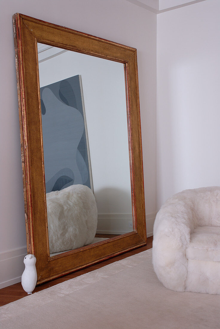 Large, wood-framed mirror showing reflection of modern painting and fluffy armchair in period apartment