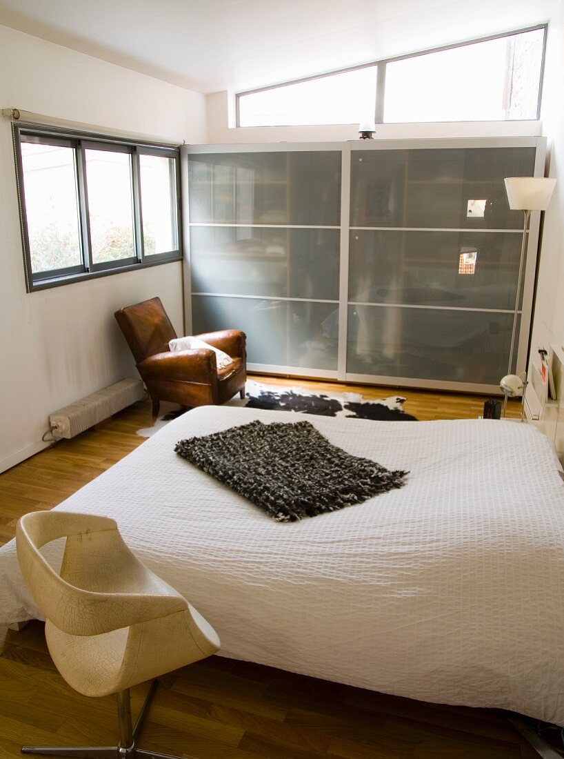 Vintage Drehstuhl neben schlichtem Doppelbett und Schrank mit Glasschiebetüren in modernem Schlafzimmer