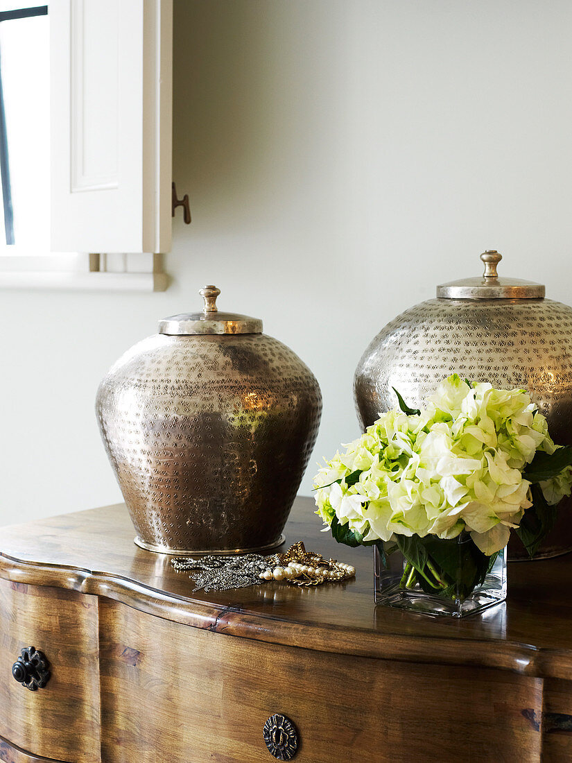 Traditional metal vessels on antique wooden chest of drawers against wall