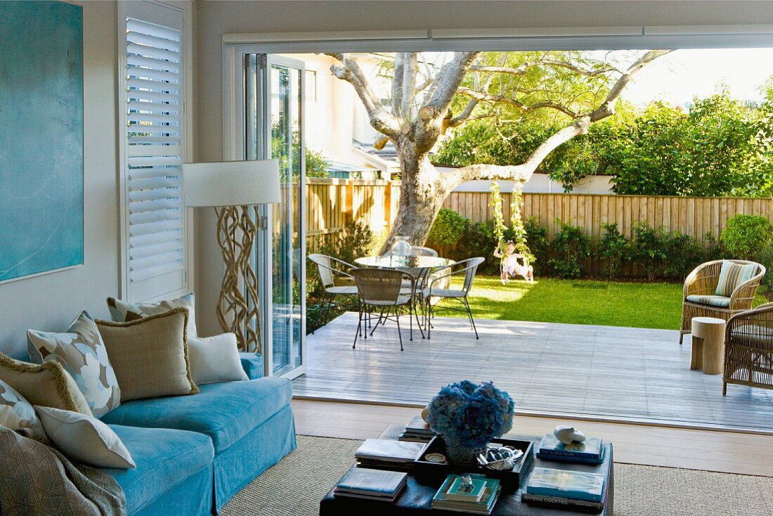 View from living room with turquoise elements to garden terrace adjoining green lawn