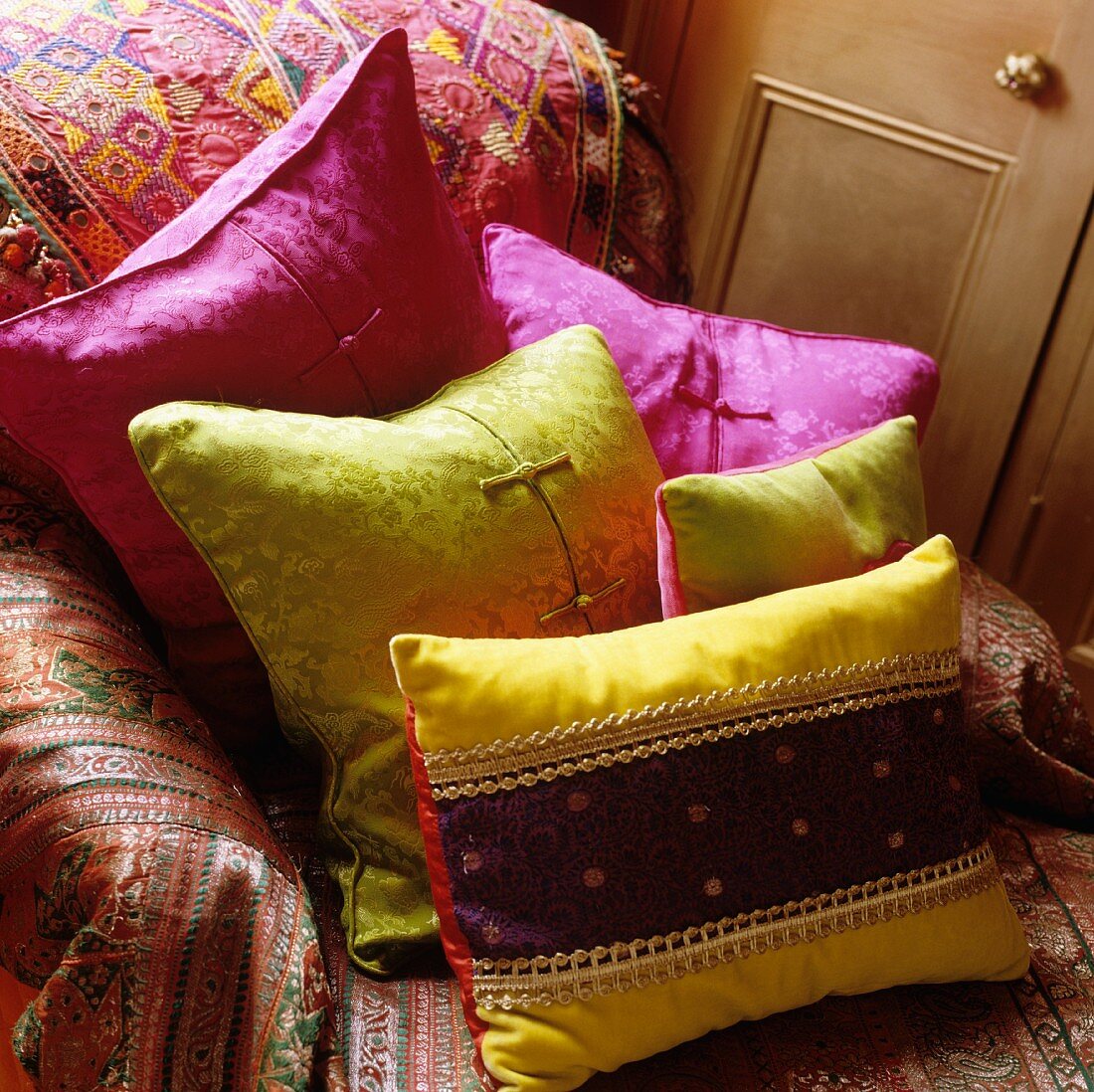 Bright satin cushions on armchair with colourful throw