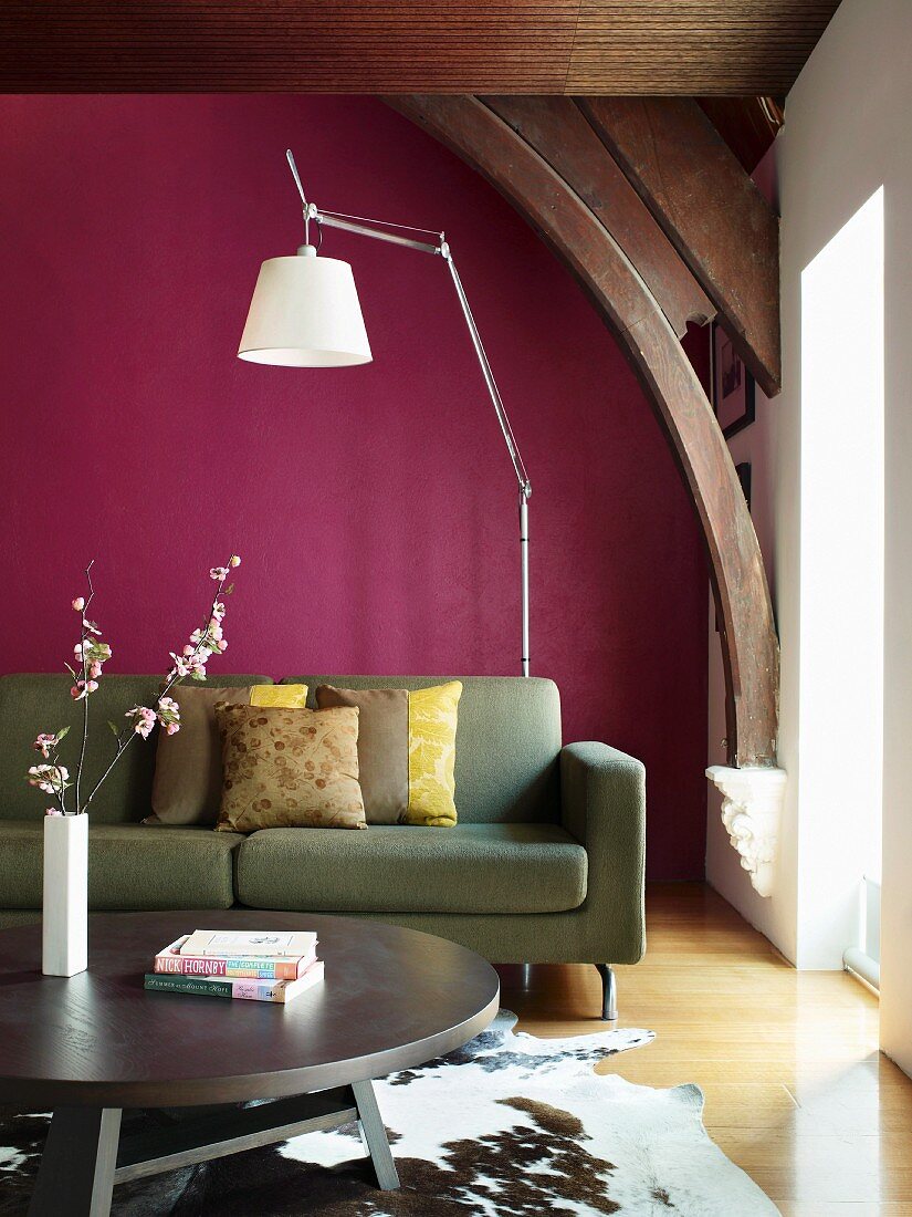 Moderne Couch vor violetter Wand unter historischen Dachbalken; im Vordergrund ein runder Couchtisch auf Tierfell
