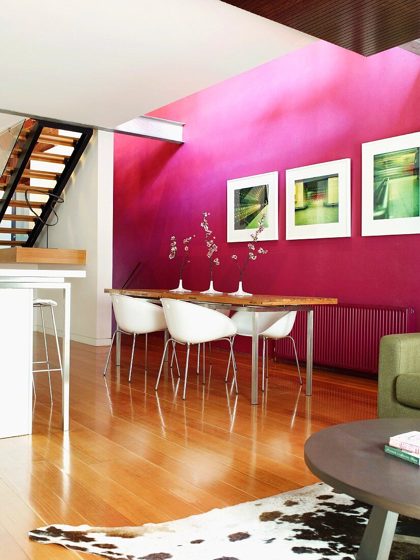 Freundlicher Essbereich mit violetter Wand, langem Esstisch mit Metallfüssen und weissen Designerstühlen