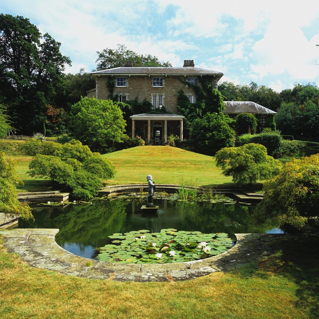 Parkähnlich angelegter Garten mit Teich vor herrschaftlichem Landhaus in sommerlicher Stimmung