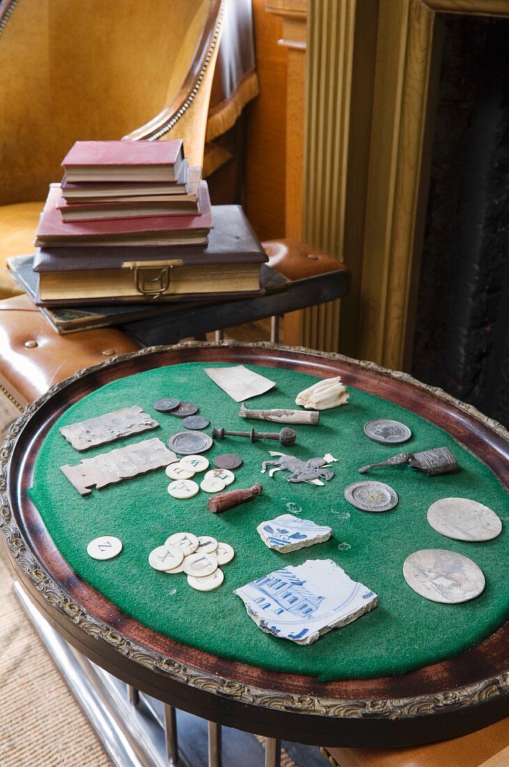 Antike Fundstücke auf gepolstertem Tablett neben Bücherstapel auf Ablage