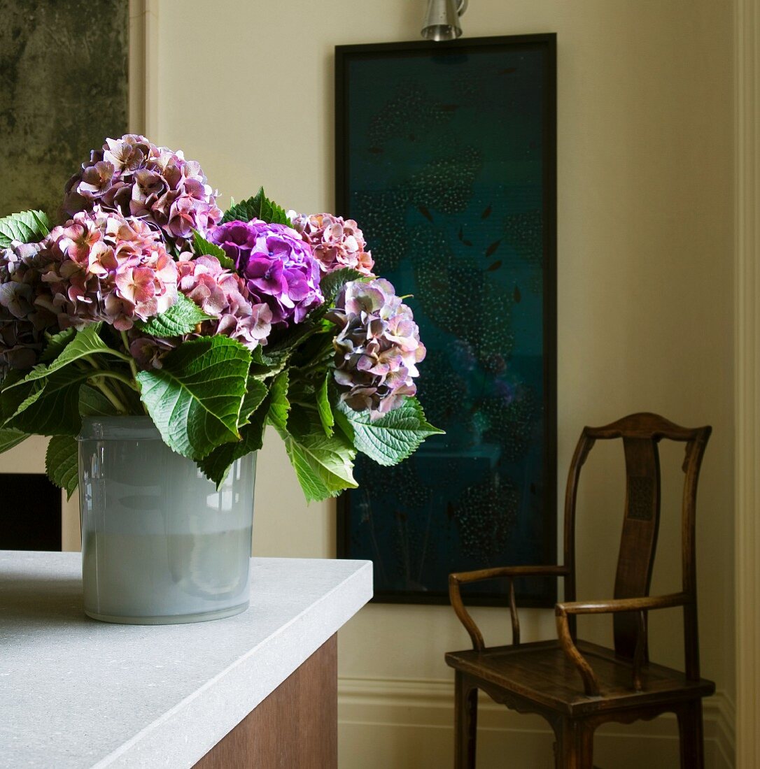 Hortensienstrauss auf der Küchenplatte; dunkelblaues Gemälde und antiker Holzstuhl im Hintergrund