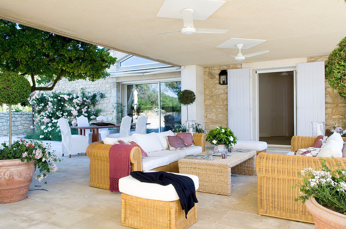 Landhaus-Terrasse mit ausladender Sofagarnitur aus Korbgeflecht und Essplatz im Hintergrund