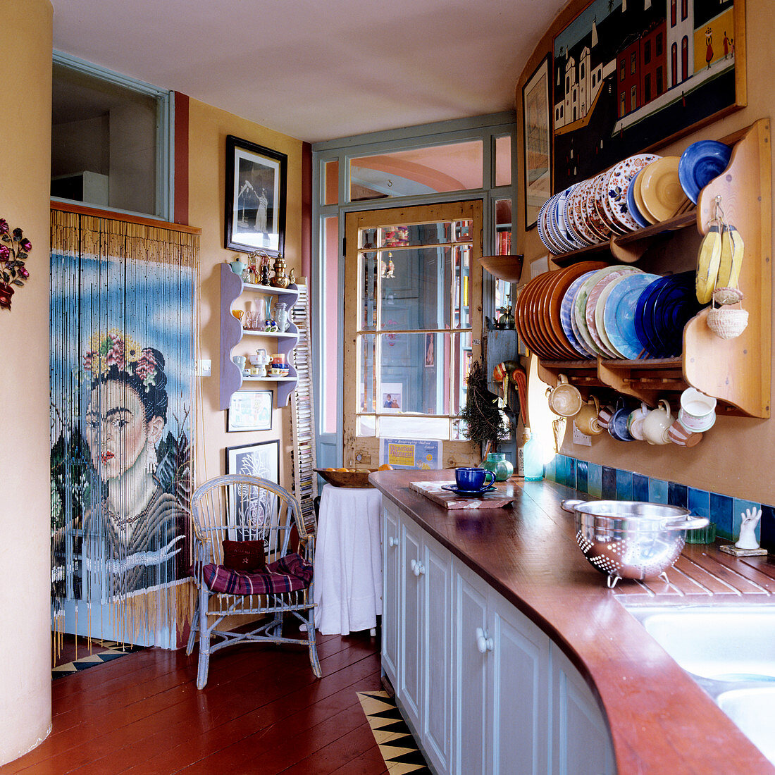 Küchenzeile unter aufgehängtem Wandbord mit Tellern gegenüber Türdurchgang und Fadenvorhang mit Portrait von Frida Kahlo