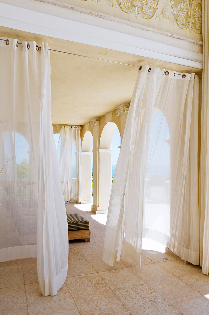 Veranda of grand villa with airy curtains hanging in front of arcade