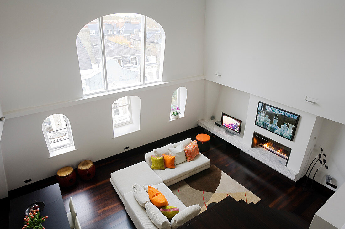 Zweigeschossiger Wohnraum in Londoner Appartement mit Blick von oben auf Rundbogenfenster und Sofa vor Gaskamin