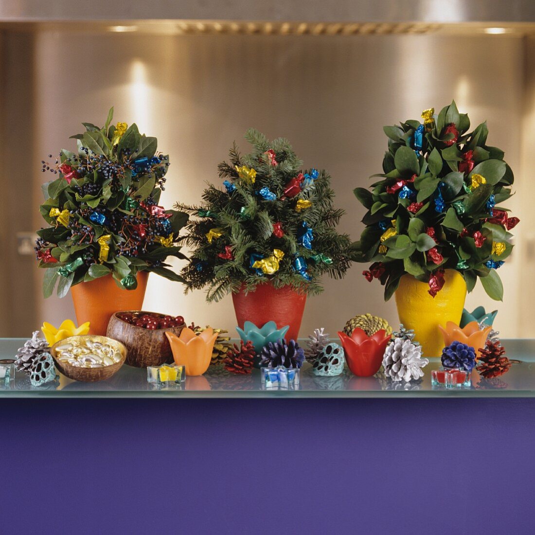 Kleine Weihnachtsbaum-Gestecke mit bunten Bonbonpäckchen und farbigen Tannenzapfen