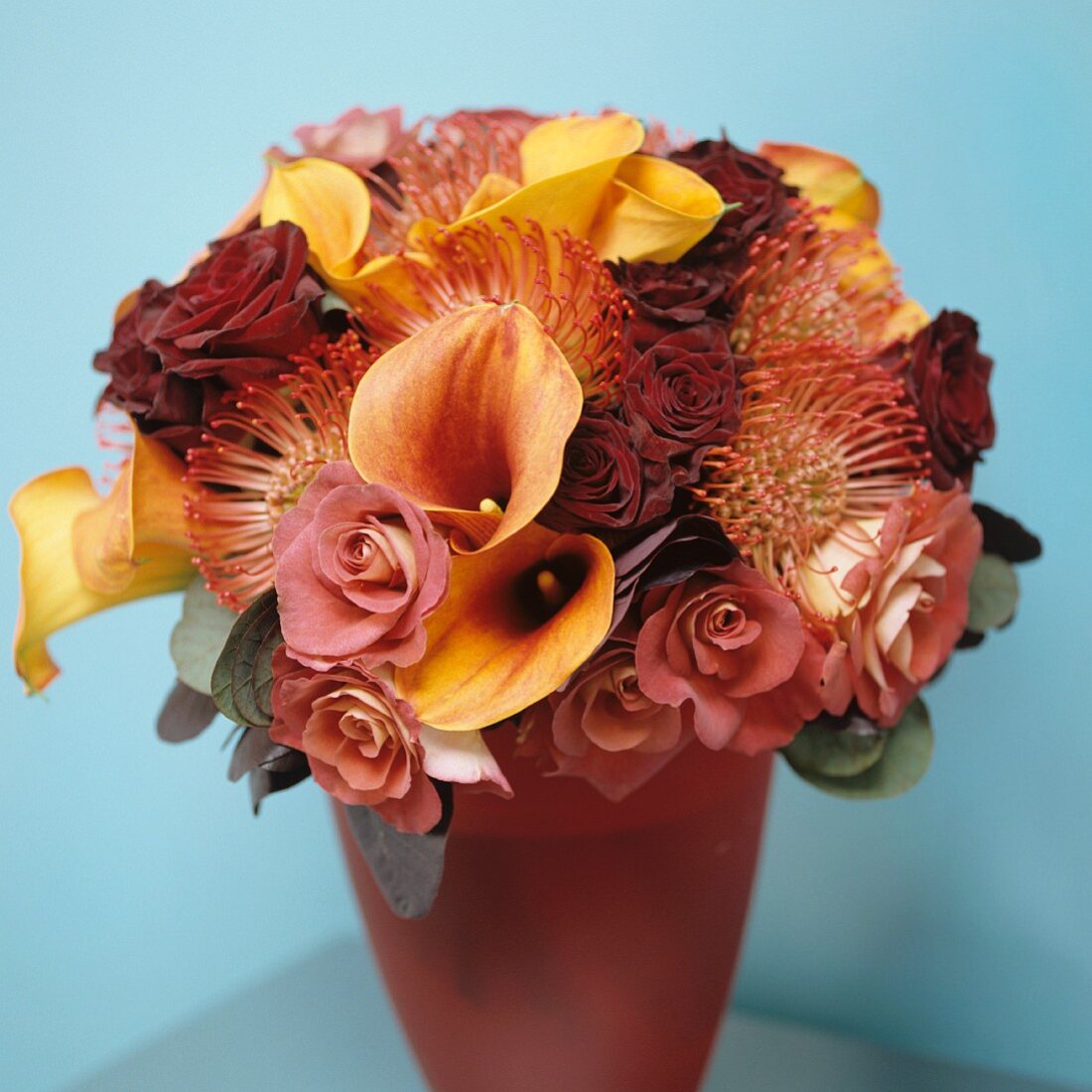 Gedeckte Rosé/Gelbtöne vor hellblauer Wand - ein kostbares Blumengebinde in farblich abgestimmter Vase