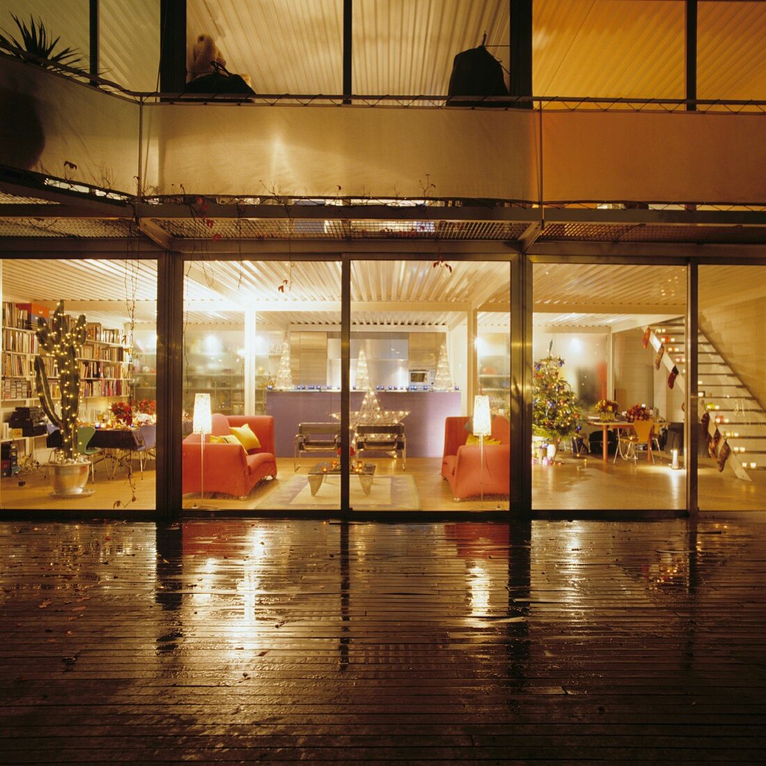 Nachtblick von regennasser Terrasse in den weihnachtlich geschmückten Wohnraum im Loftstil
