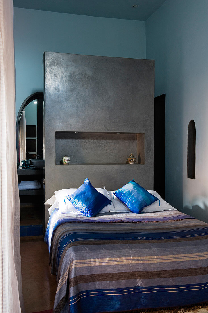 Moroccan bedroom with striped bedspread on bed against grey-painted partition