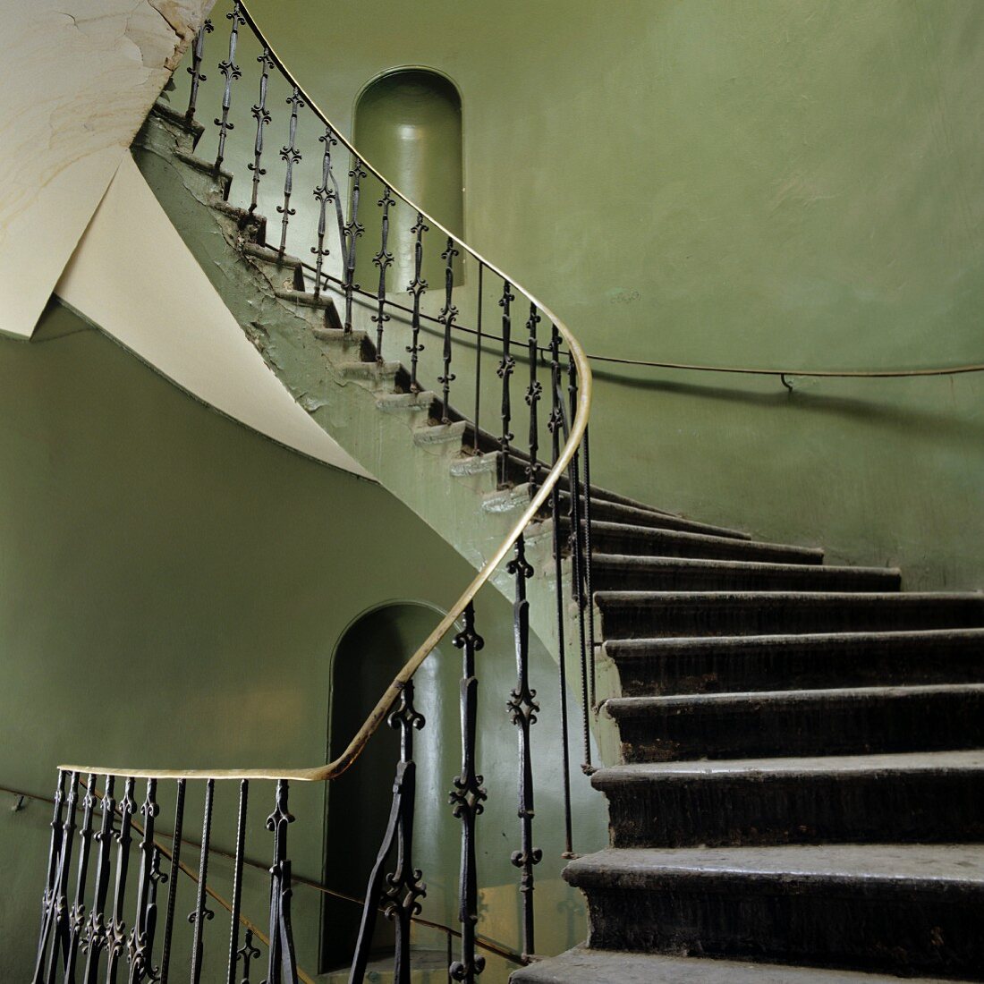 Vintage stairwell - spiral staircase with wrought iron balustrade and niches in gray-green painted walls
