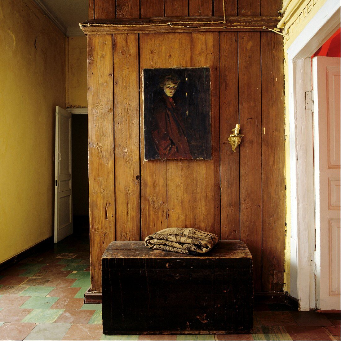 Alte Truhe vor Holzwand mit Gemälde in schlichtem Hausflur