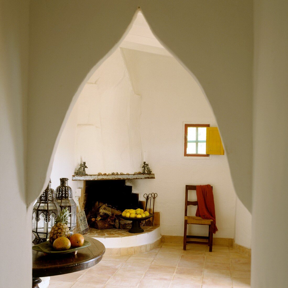 Blick durch orientalischen Spitzbogen auf offenem Kamin in schlichtem Zimmer