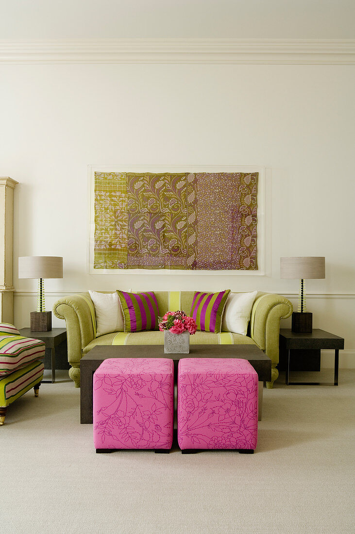 Elegantes Wohnzimmer im Art-Deco-Stil - Pinkfarbene Polsterhocker und traditionelles Sofa zwischen Beistelltischen mit Tischlampe