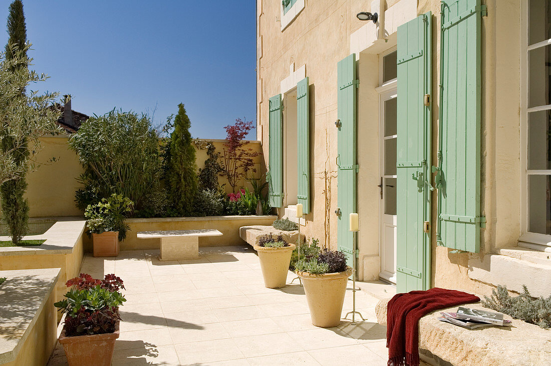 Sonnige Terrasse mit Pflanzentöpfen vor mediterranem Wohnhaus