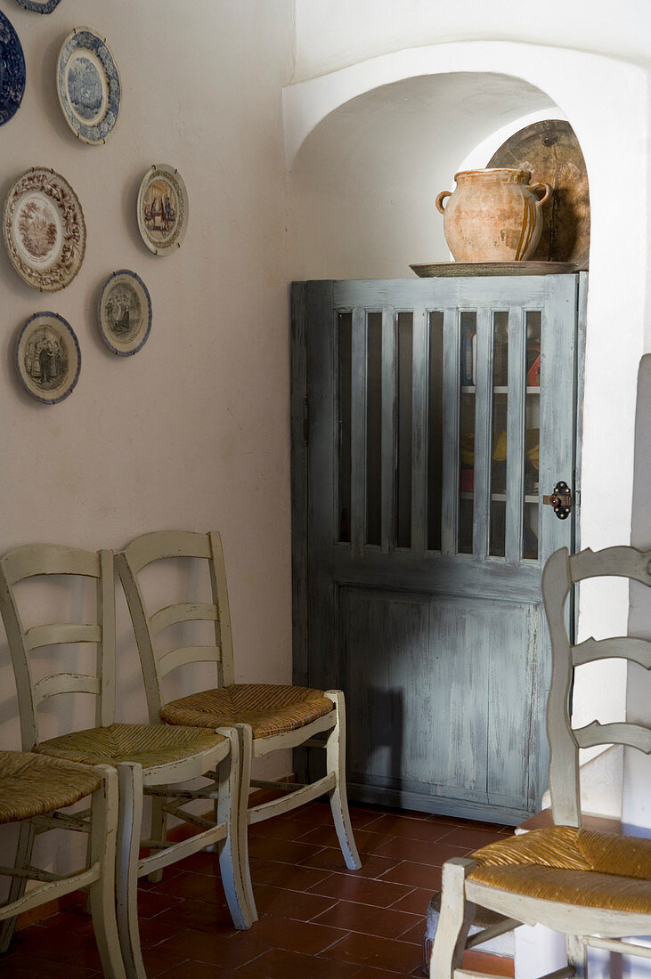 Küchenstühle an Wand unter gehängten Wandtellern und rustikale Holztür vor Einbauschrank in mediterraner Esszimmerecke