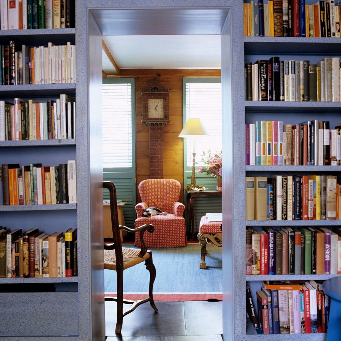 Open doorway in bookcase showing view of country-style armchair