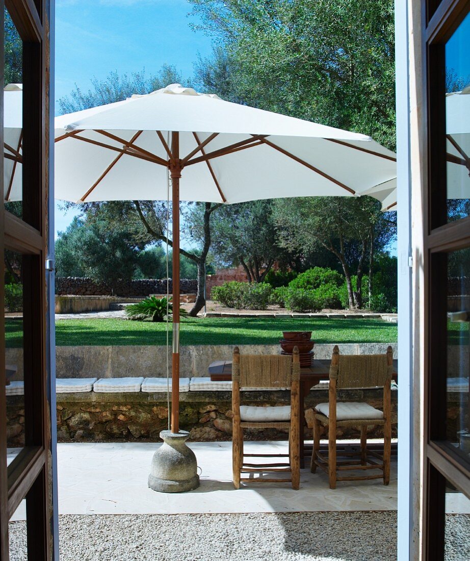 Blick durch offene Tür auf Terrassenplatz mit Sonnenschirm und Garten