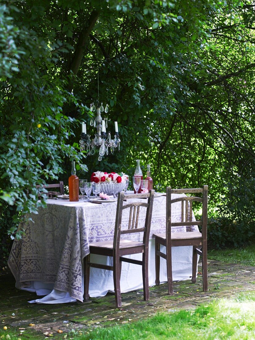 Dunkle Holzstühle vor Tisch mit Tischtuch im Garten