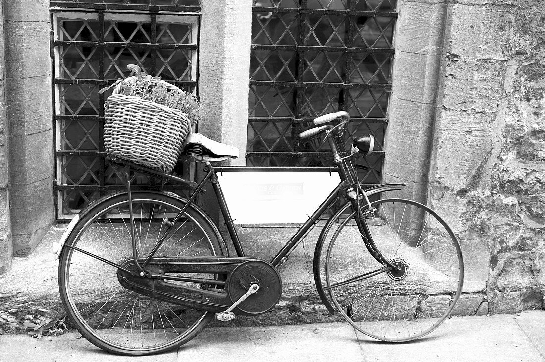 Altes Fahrrad mit Korb an Hauswand gelehnt (Schwarz-Weiß-Aufnahme)