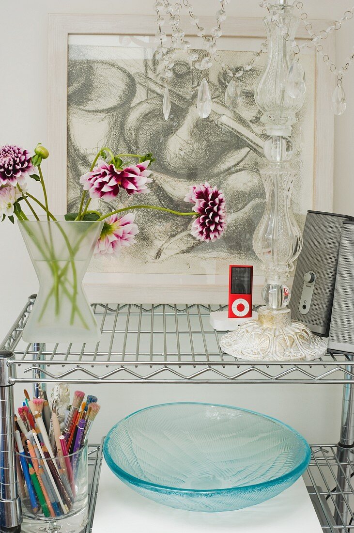 Dahlias, speakers and glass of pencils on chrome shelf in front of framed drawing