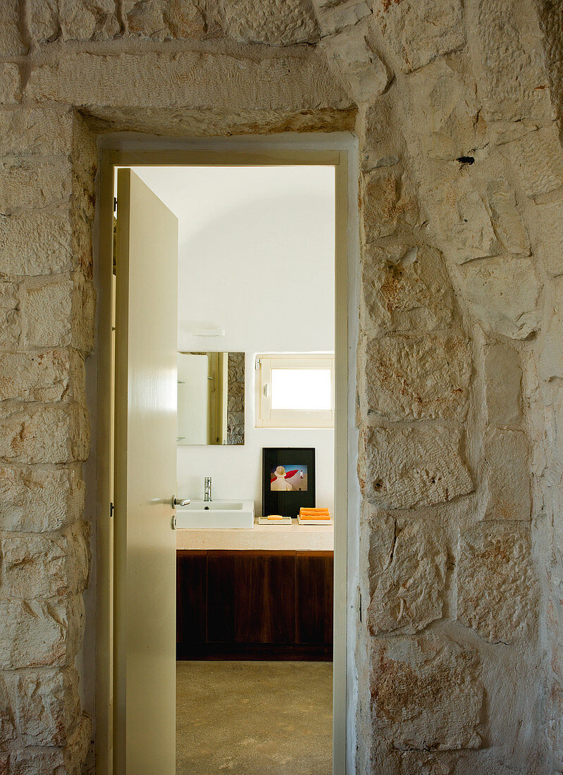 Vorraum mit Naturstein Wand und Blick durch offene Badtür auf modernen Waschtisch