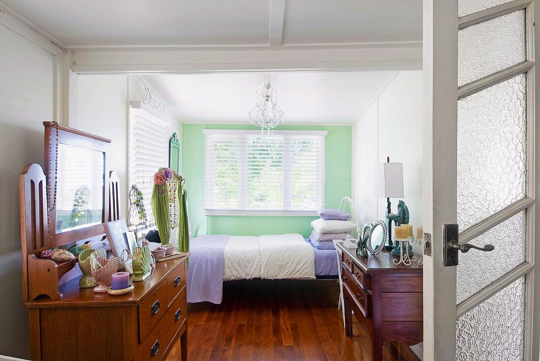 Schlichtes Zimmer mit antikem Schminktisch an Wand und Bett am Fenster