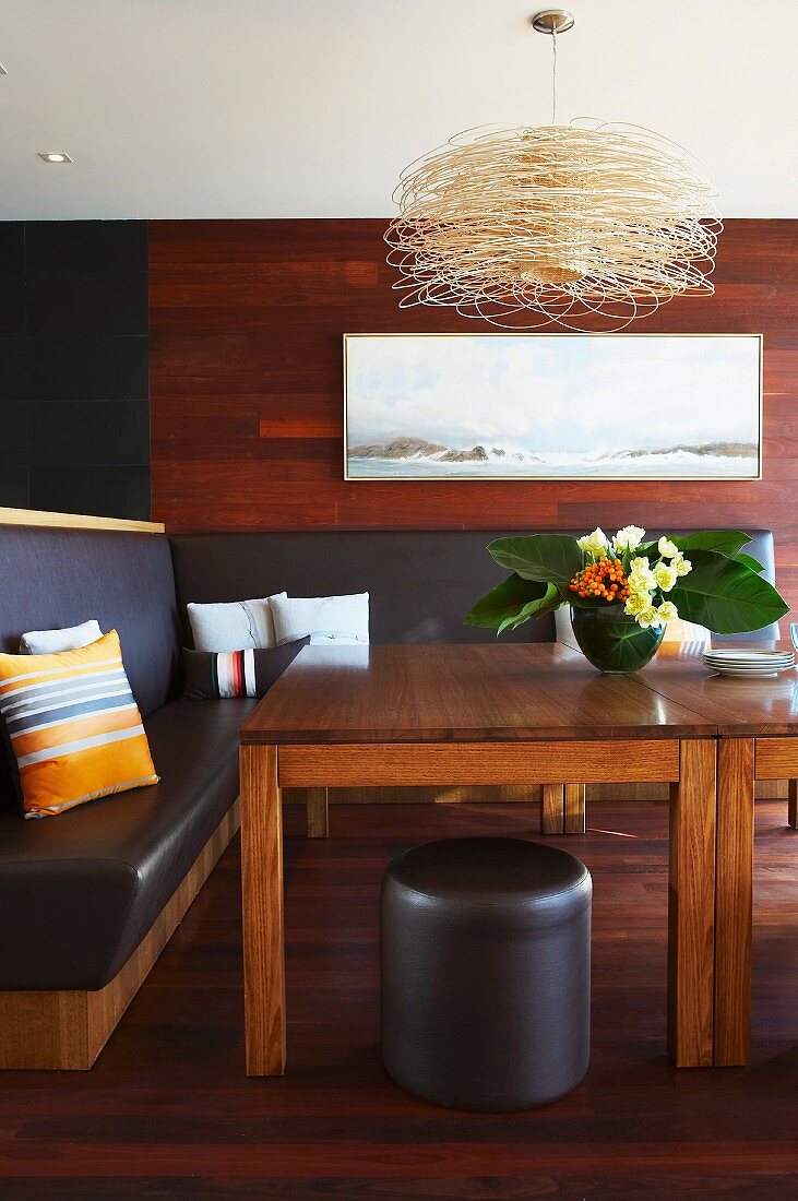 Eckbank mit schwarzem Lederpolster und Holztisch in Esszimmer mit Holzbelag auf Wand und Boden