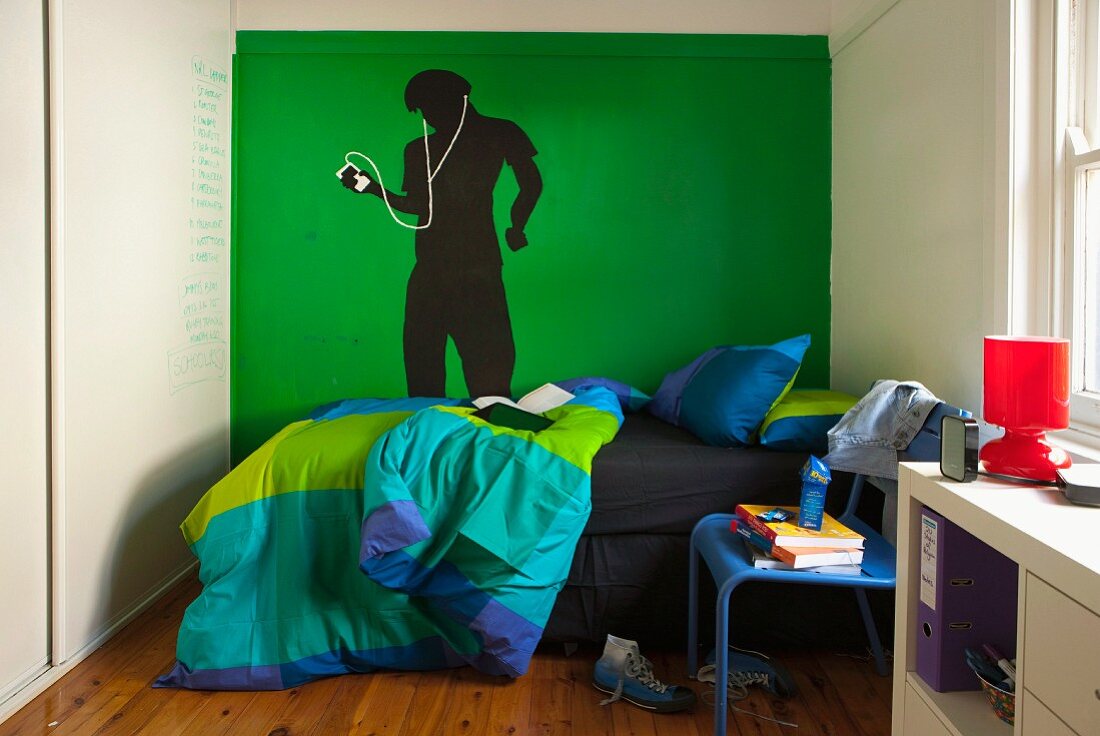 Jugendzimmer mit Bett vor grüner Wand und gemalter Figur