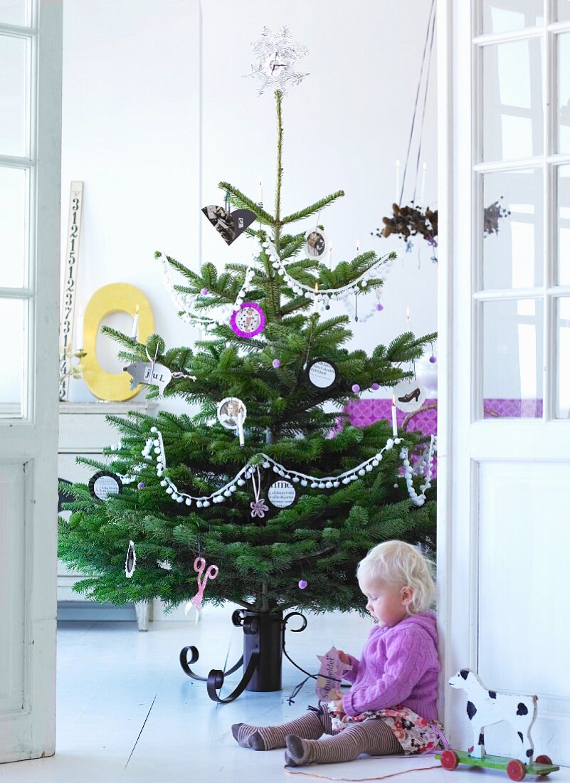 Kind sitzt vor geschmücktem Weihnachtsbaum auf Boden
