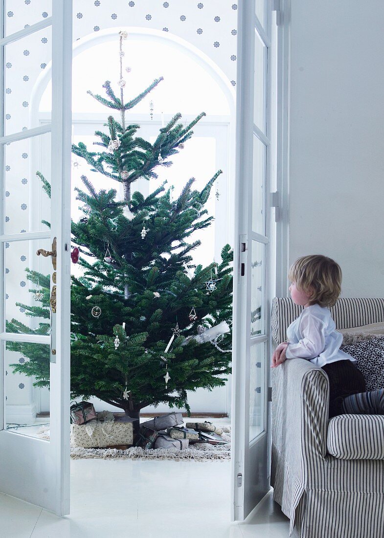 View of Christmas tree through open double doors and child on sofa