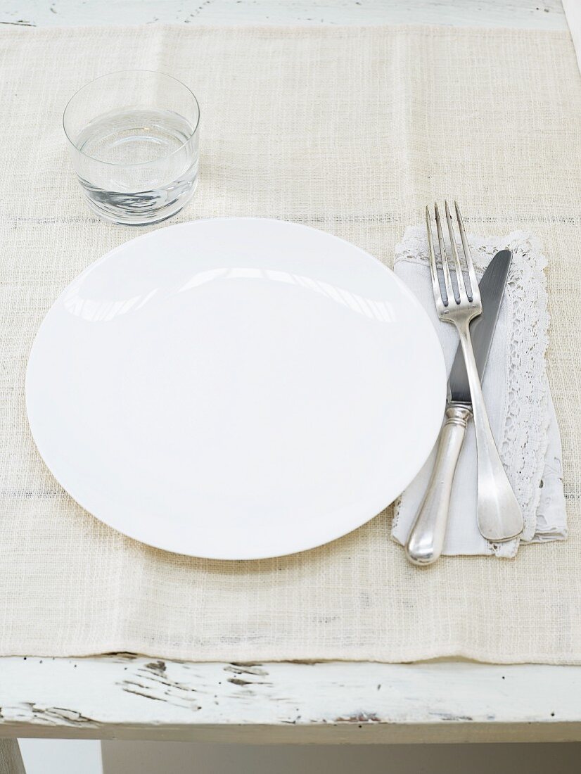 Gedeck mit weißem Teller, Besteck und Wasserglas