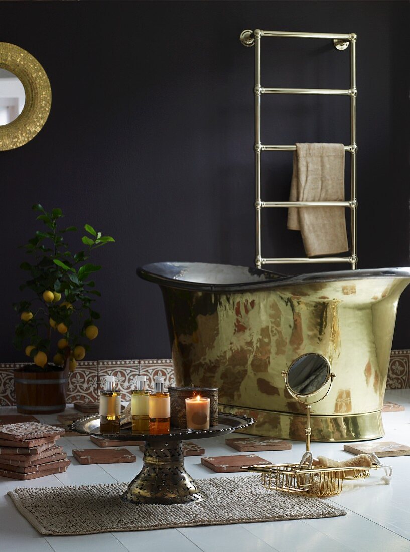 Bad mit orientalischem Flair - brennende Kerzen auf Beistelltisch aus Messing und golden glänzende Badewanne