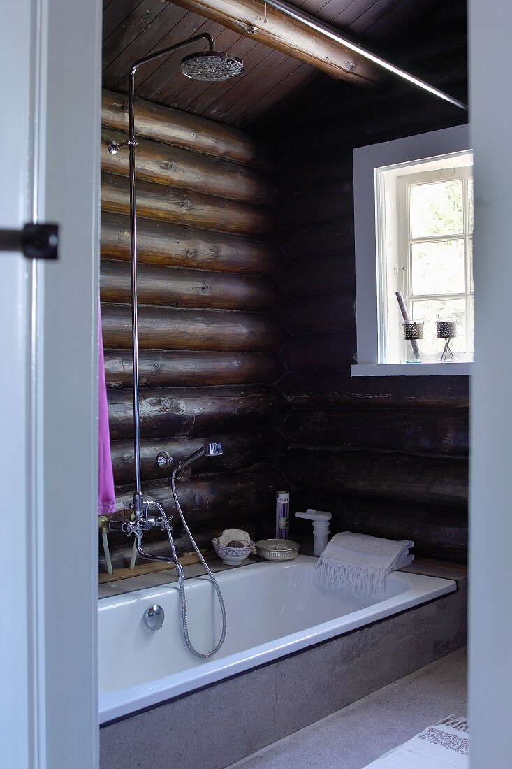 Modernes Bad im Blockhaus - in Boden eingelassene Badewanne vor Holzbohlenwand