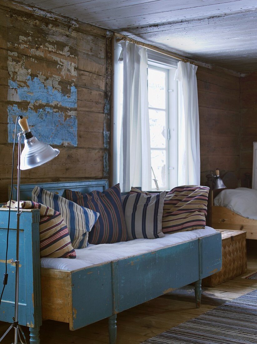 Rustikales Sofa mit Kissen vor Holzwand mit abblätternder Farbe
