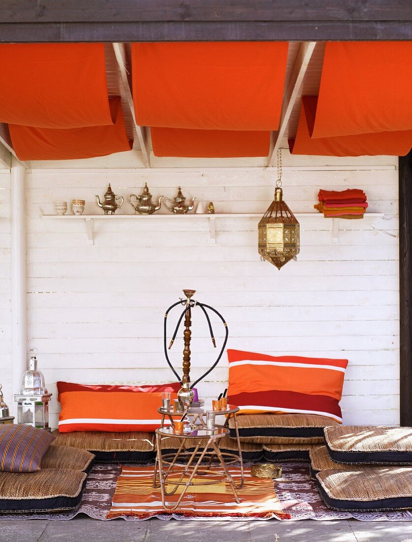 Chill-out area in Oriental-style living room with floor cushions below orange awnings on ceiling
