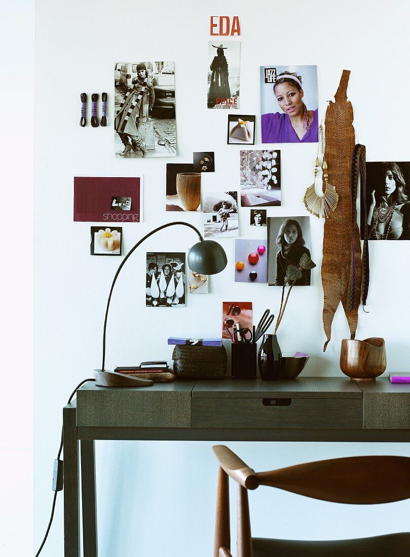 Moderner Schreibtisch aus dunklem Holz vor Wand mit angehefteten Photos