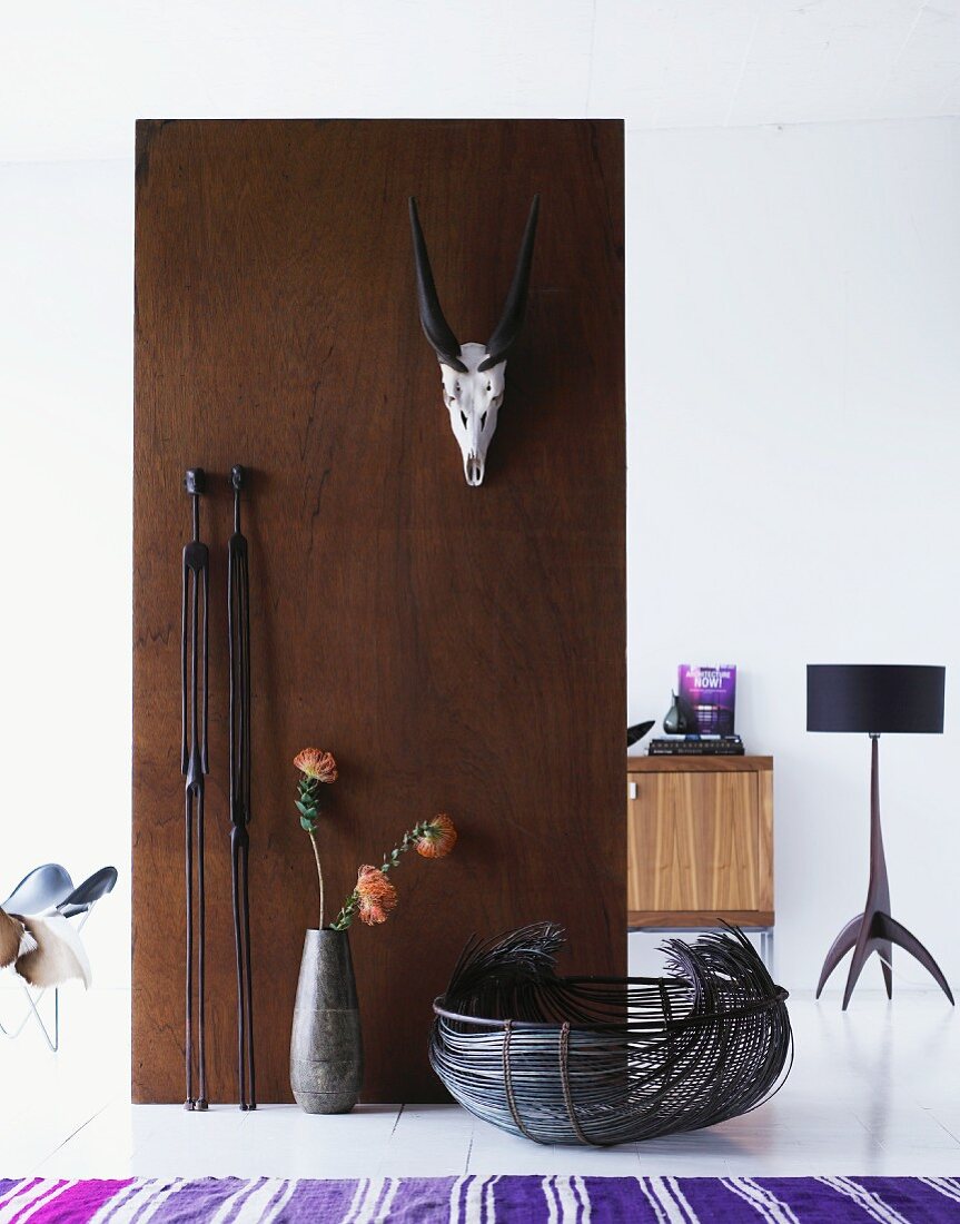 Raumteiler aus Holz mit gehängter Tiertrophäe und Blick in Wohnraum auf Stehlampe