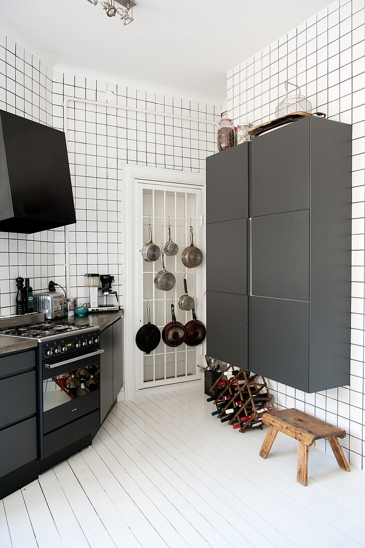 Black and white designer kitchen - black cupboards on walls tiled from floor to ceiling and white wooden floor