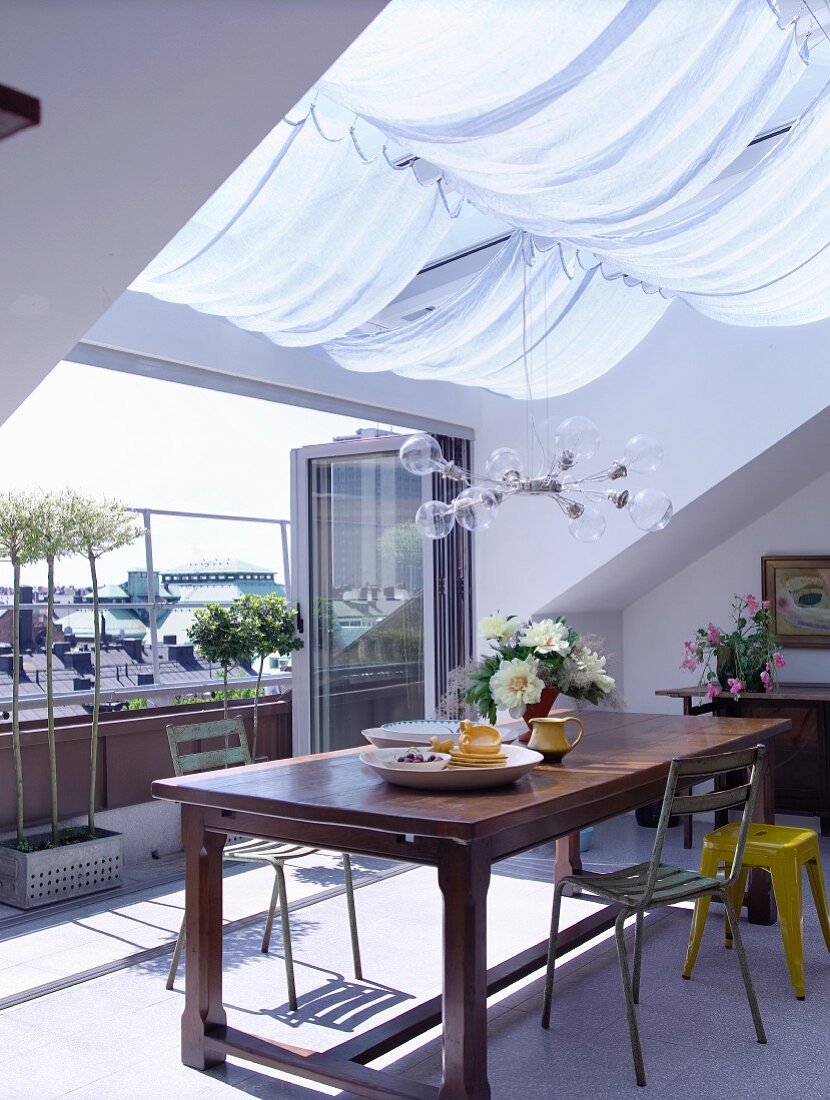 Essplatz unter Dachfenster mit Sonnensegel und offenen Falttüren vor Terrasse