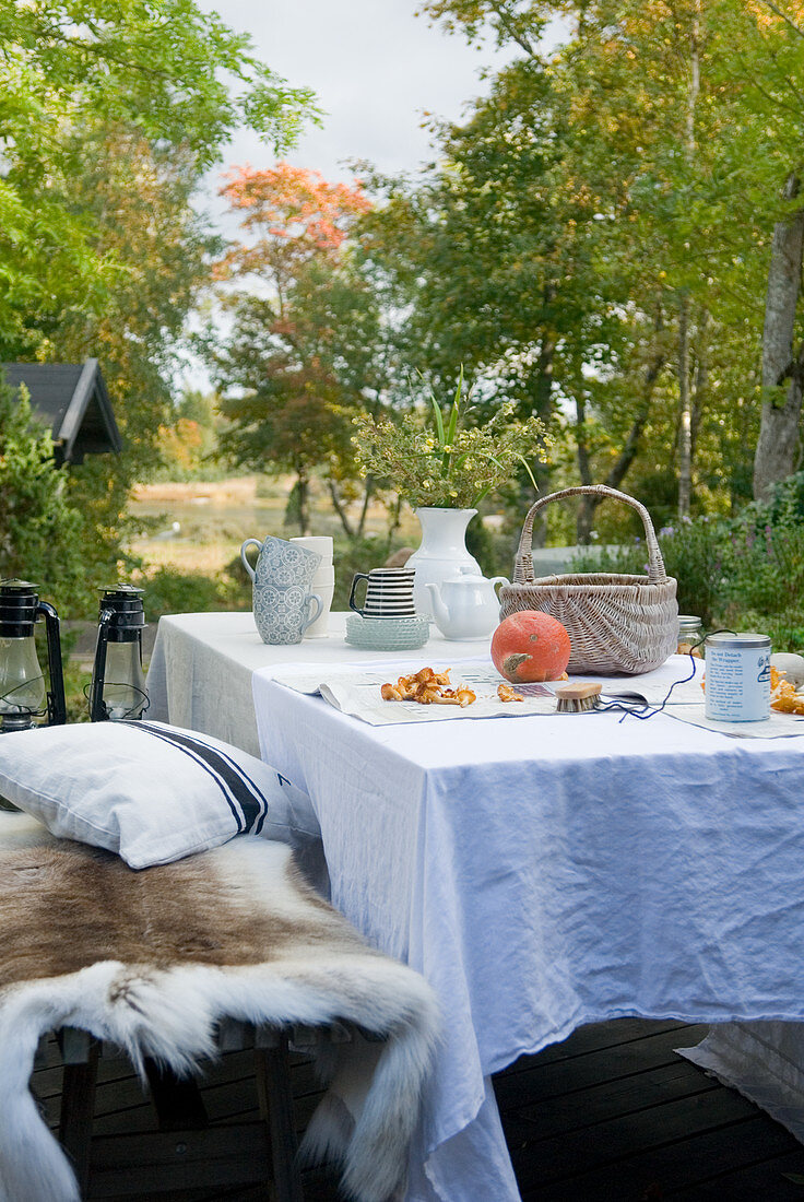Herbstlicher Tisch mit weisser Tischdecke und Bank mit Tierfell im Freien