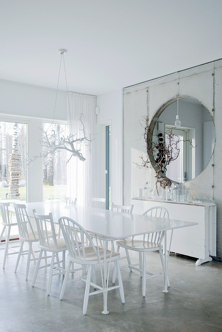 Tisch mit 30er Jahre Designerstühlen in weißem Esszimmer und Raumteiler aus Sichtbeton mit kreisförmiger Öffnung