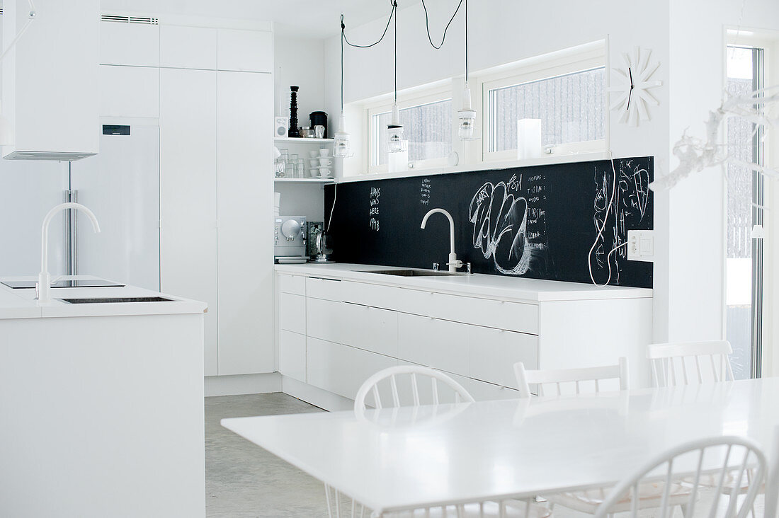 Offene Designerküche in puristischem Weiß mit schwarzem Spritzschutz