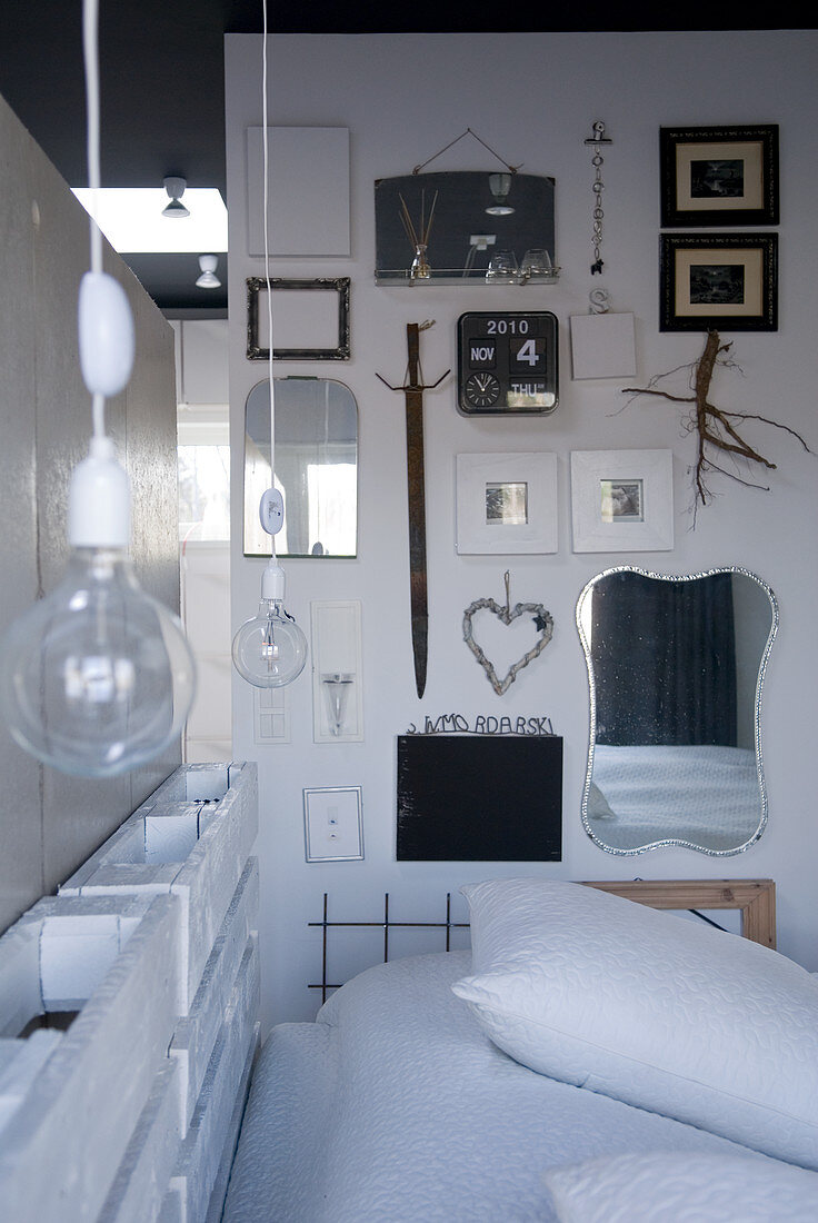 Puristischer Schlafplatz mit Europaletten und Glühbirnen am Kopfende; gesammelte Rahmen und Spiegel an der seitlichen Wand
