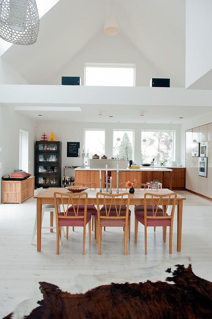Esstisch und Stühle aus Holz im 50er Jahre Stil vor Küchenbereich und Blick auf die Galerie in offenem Wohnhaus